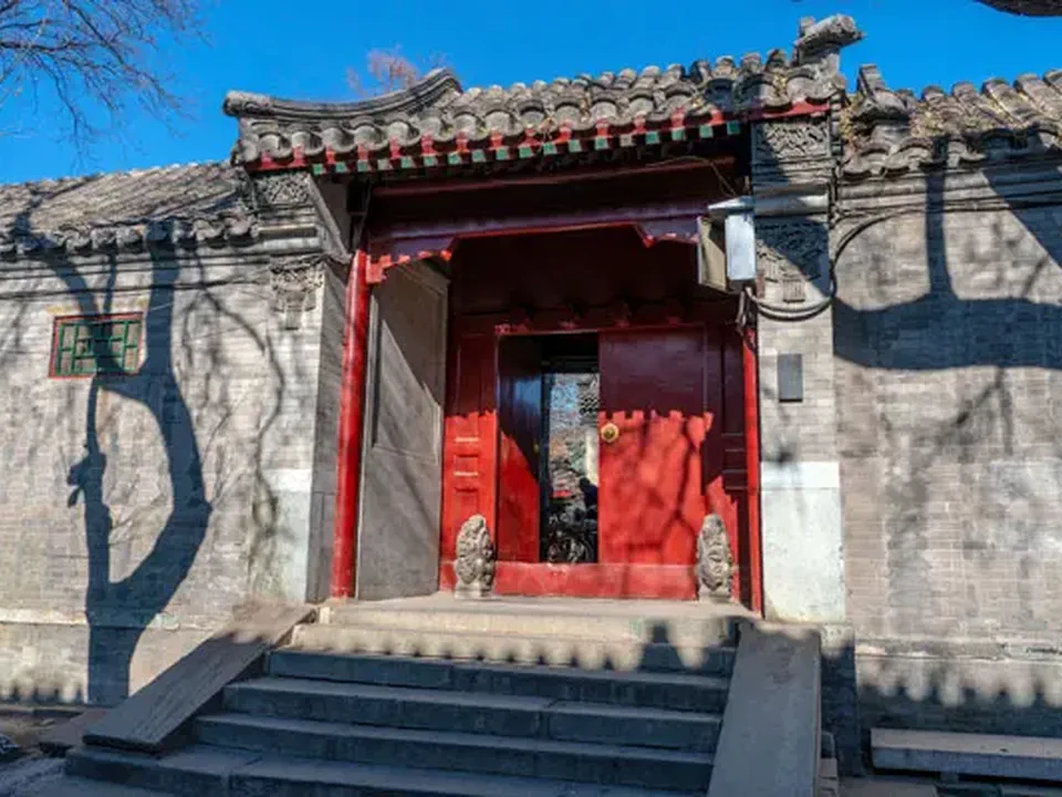 A red courtyard gate in a sunlit Beijing hutong